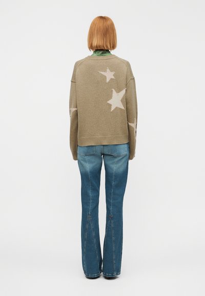 Πράσινο ελιάς πουλόβερ με ροζ αστέρια, σε oversized γραμμή, με ριμπ μανσέτες, συνδυασμένο με καμπανέ τζιν σε μπλε χρώμα, ελαφρώς ξεβαμμένο.