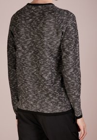 Pull en tricot texturé noir et gris avec des manches longues, un col rond et un ourlet noir contrastant. Présente un motif en tricot sur l'ensemble.