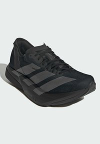 Black athletic shoe with a mesh upper, textured accents, flat laces, and three reflective stripes on the side. Features a cushioned sole.