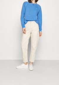 Sudadera azul claro con cuello redondo y detalles acanalados, combinada con pantalones blancos roto ajustados y zapatillas blancas.