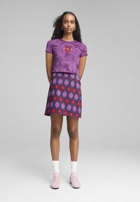 Fioletowy crop top w tie-dye z czerwonym haftem, połączony z granatową spódnicą z czerwonymi i różowymi wzorami kwiatowymi. Różowe sneakersy dopełniają stylizację.