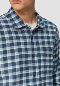 Blauwe geruite flanellen shirt in verschillende tinten blauw en wit, met een kraag, knoopsluiting en een borstzak. Zachte textuur.