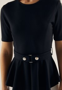 Černý přiléhavý top s kulatým výstřihem a krátkými rukávy, s rozšířeným peplum lemem a ozdobným páskem se stříbrným kováním.