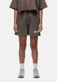 Bruine katoenmix shorts met een elastische tailleband, voorzien van een logo-opdruk. Gecombineerd met een losvallend bruin bovenstuk en grijze sportschoenen.