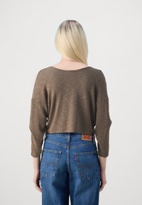 Crop top beige côtelé à manches trois quarts, associé à un jean denim bleu taille haute avec poches arrière et patch logo.