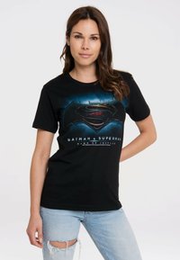 Black cotton t-shirt featuring a Batman vs. Superman graphic in blue and red hues, with "Dawn of Justice" text printed below.