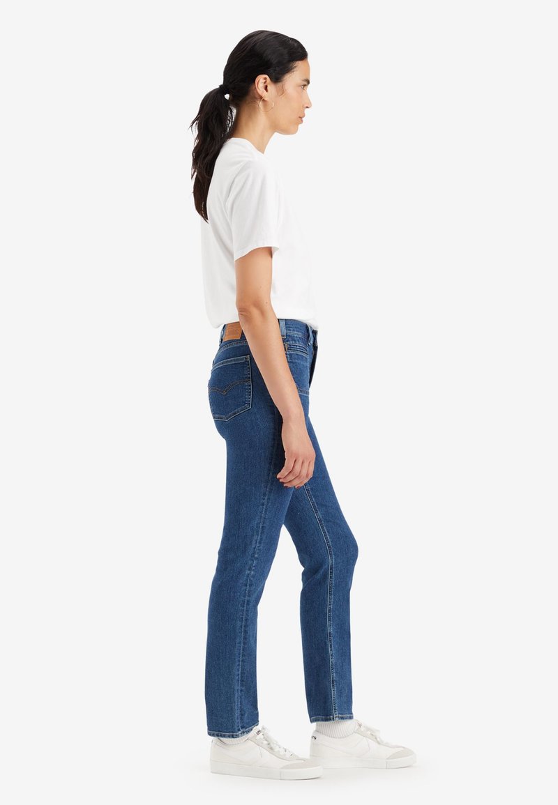 Jean en denim bleu avec une coupe droite, taille haute et poches arrière. Assorti à un t-shirt blanc uni et des baskets blanches.
