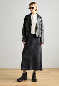 Svart läderjacka i bikerstil över en vit tröja, kombinerad med en lång svart jeanskjol och svarta ankelstövlar med tjocka sulor.