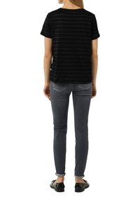 Schwarz gestreiftes T-Shirt mit kurzen Ärmeln, runder Ausschnitt, lässige Passform, kombiniert mit grauen Jeans und schwarzen Schuhen, von hinten betrachtet.