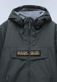 Mørkegrøn polstret jakke med hætte, der har en grå fleece-foring, frontlynlås og et fremtrædende logo-patch. Lynlåslukket sidelommer.