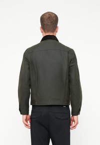 Πράσινο σακάκι με κοτλέ γιακά, κουμπωτές μανσέτες και ραμμένη γραμμή. Φτιαγμένο από μια υφασμάτινη υφή, διαθέτει τσόχες στο πίσω μέρος και παστούς. 