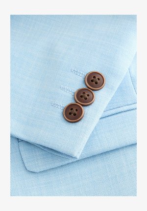 Hellblaues Gewebe mit einer strukturierten Webart, das drei braune Knöpfe mit vier Löchern auf einer gefalteten Kante des Materials zeigt.