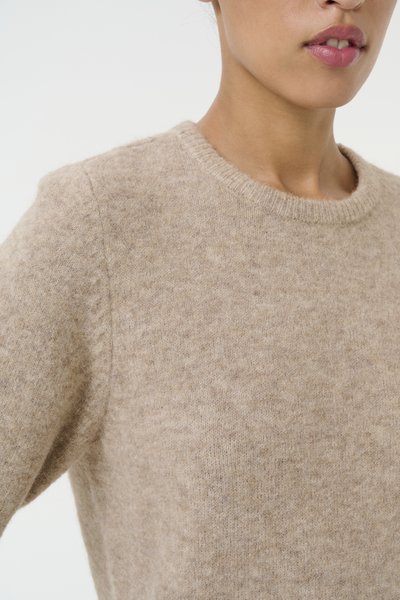 Pull en laine beige avec un col rond et des finitions côtelées ; il présente un tissu doux et texturé ainsi qu'une coupe décontractée.