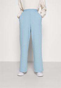 Hellblaue, rautenstrukturierte Hosen mit lockerer Passform, die einen elastischen Bund und Seitentaschen besitzen. Kombiniert mit weißen Sneakers.