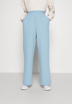 Pantalons à texture gaufrée bleu clair avec une coupe décontractée, dotés d'une taille élastique et de poches latérales. Associés à des baskets blanches.