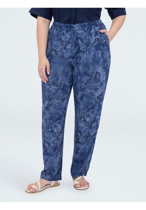 Persona que lleva puestos pantalones azules con estampado floral, de corte relajado, con cintura elástica y sandalias blancas de punta abierta.