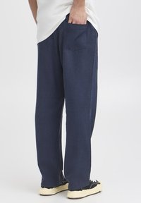 Námořnicky modré široké kalhoty z měkké látky s zadní kapsou, kombinované s černými botami a světlou košilí.
