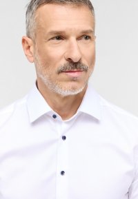 Witte dress shirt met een textuurafwerking, een gespreide kraag en donkerblauwe knopen. De stof lijkt soepel en goed passend.