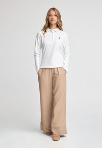 Vit långärmad polo skjorta med krage och knäppning fram, matchad med vida beige byxor och bruna skor. Enkelt mönster och passform.