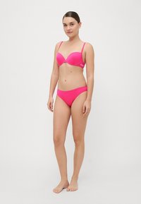 Růžový bikini set obsahující vyztuženou push-up podprsenku s nastavitelnými ramínky a odpovídajícími nízkými kalhotkami, hladkou texturu a bez viditelných vzorů.