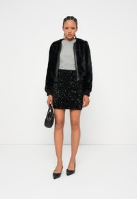 Casaco bomber de pele sintética preta, t-shirt cinza e saia mini de lantejoulas pretas. Acessórios incluem uma bolsa preta e sapatos de bico fino.