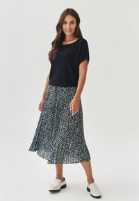Haut en tricot marine à manches courtes associé à une jupe midi florale avec un fond sombre et des motifs bleu clair et blanc. Chaussures blanches à enfiler.