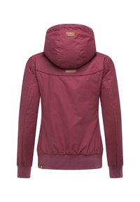 Veste à capuche bordeaux avec des poignets et une taille élastiques, présentant une texture de tissu lisse et un patch logo au dos.