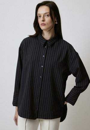 Black striped button-up shirt with a collar, loose fit, wide sleeves, and purple buttons. Smooth fabric with a subtle sheen.