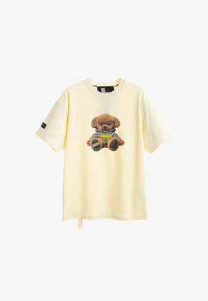 Joven vestido con camiseta crema con estampado de oso de peluche, pantalones cortos vaqueros azules con detalle de oso, calcetines blancos con estampado, y zapatos beige sin cordones.