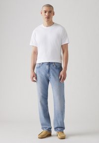 Hvit bomulls t-skjorte, lyseblå rette jeans og brune mokasinstil sko. Enkelt design uten synlige mønstre eller logoer.