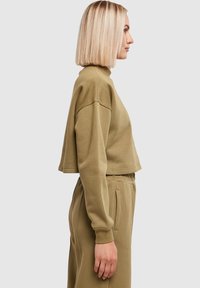 Olivengroene cropped trui met een hoge hals, losse pasvorm en geribde manchetten. Gladde textuur, gecombineerd met bijpassende broek met elastische taille.