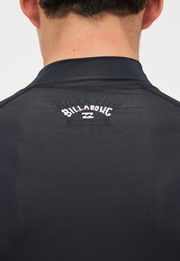 Czarna koszulka z długim rękawem, wykonana z teksturowanej tkaniny, o dopasowanym kroju, z białym logo "Billabong" na górnej części pleców.