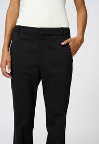 Czarne eleganckie spodnie o gładkiej fakturze, z bocznymi kieszeniami i dopasowanym stanem. Materiał jest lekki i elastyczny.