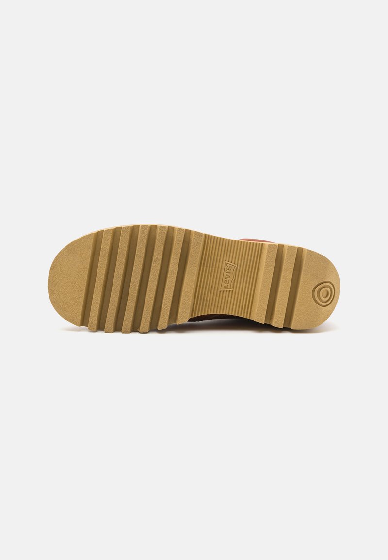 Suela de sneaker de goma marrón con un patrón texturizado y acanalado. Marca prominente en el lateral y detalle circular en el talón.