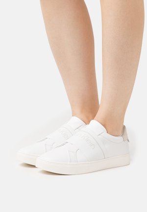 Sneaker bianchi con fasce elastiche, accenti beige e superficie in pelle liscia. Presentano un profilo basso e un design a punta arrotondata.