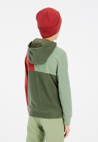 Fleece hoodie i rød, grøn og olivengrønne paneler; har en hætte og ribbede manchetter; parret med lysegrønne bukser.