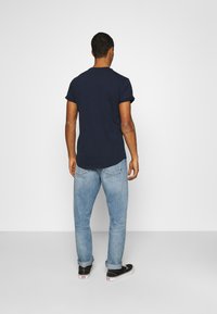 Navyblaue Baumwoll-T-Shirt mit umgeschlagenen kurzen Ärmeln, kombiniert mit hellblauen Jeans. Schwarze Schuhe mit weißen Sohlen, lässige Passform.
