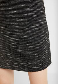 Czarna i biała spódnica w wzory, charakteryzująca się teksturowanym materiałem z cienkimi poziomymi liniami, zaprojektowana w prostym kroju i z końcem na wysokości połowy uda.