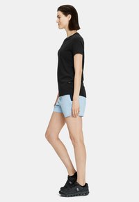 Camiseta negra de manga corta combinada con pantalones cortos de un azul claro. Modelo lleva zapatillas deportivas negras; diseño minimalista, textura de tela suave.
