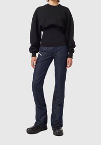 Černý nadměrný svetr s žebrovaným pasem, v kombinaci s tmavě modrými džíny s rovnými nohavicemi a černou odolnou obuví.