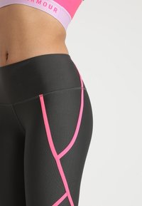 Leggings de sport noirs avec des accents roses, présentant un design ajusté, un tissu texturé et des détails de coutures distinctifs qui sculptent les jambes.