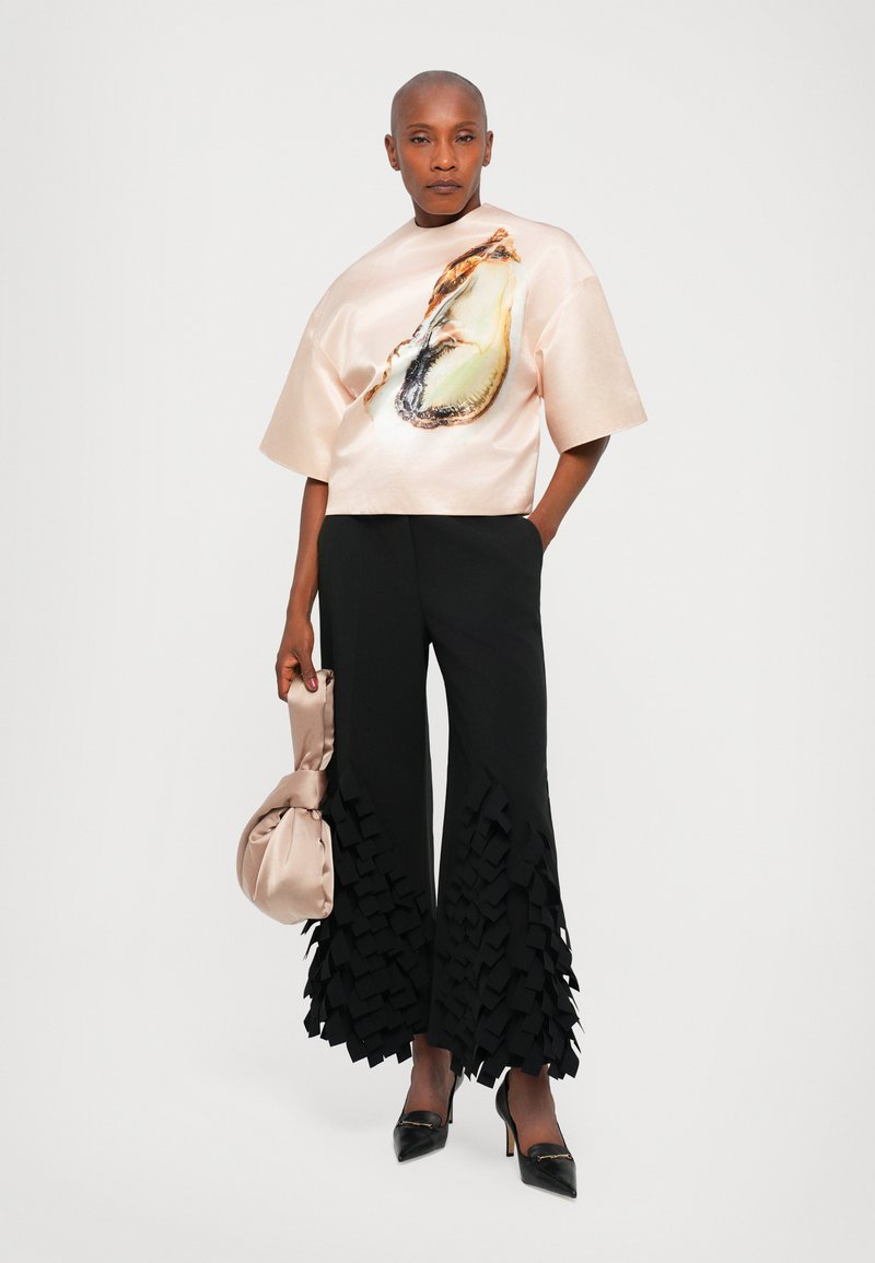 Zijde top met oesterafbeelding, brede zwarte broek met gelaagde ruffle zooms, en een satijnen pouch tas. Zwarte puntige hielen maken de look compleet.