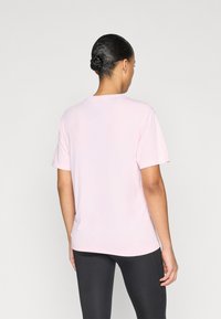 Ροζ κοντομάνικη μπλούζα από απαλό ύφασμα. Απλός σχεδιασμός με στρογγυλή λαιμόκοψη και ελαφρώς φαρδιά εφαρμογή. Διακρίνονται μαύρα κολάν.