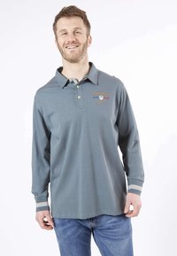 Polo à manches longues en coton bleu clair avec un col. Présente des coutures décoratives et une bordure à motifs visible au niveau du col.