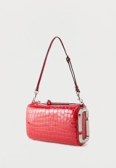 Κόκκινη ορθογώνια τσάντα με υφή κροκόδειλου, με ένα ιμάντα και ασημένιες μεταλλικές λεπτομέρειες στο πλάι, σε ένα μονόχρωμο φόντο.