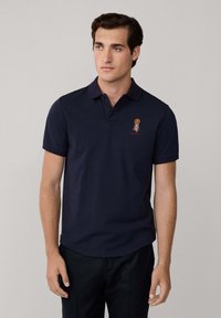 Marinblå polo skjorta i bomull med krage med två knappar, med en liten broderad logotyp på bröstet och uppvikt ärmar.