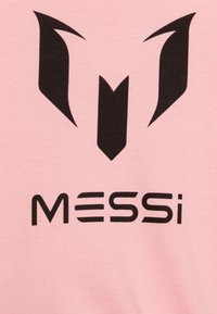 Ružové tričko s výrazným čiernym logom nad textom "MESSi" v tučných čiernych písmenách. Hladká štruktúra látky.