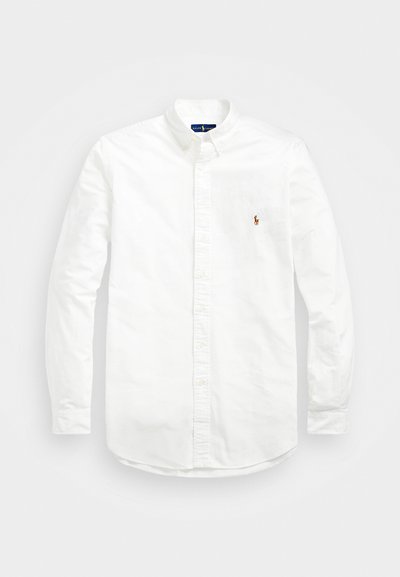 Chemise blanche à manches longues en coton avec un col boutonné, ornée d'un petit logo brodé rouge et marine sur le côté gauche de la poitrine.