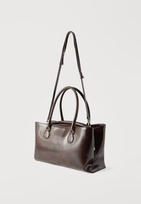 Σκούρα καφέ ορθογώνια δερμάτινη τσάντα χειρός με διπλές λαβές στο επάνω μέρος και ρυθμιζόμενο ιμάντα ώμου σε λευκό φόντο.