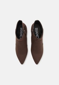 Brown suede ankle boots with pointed toes and side zippers. Interior features brand logo in white on a black insole.